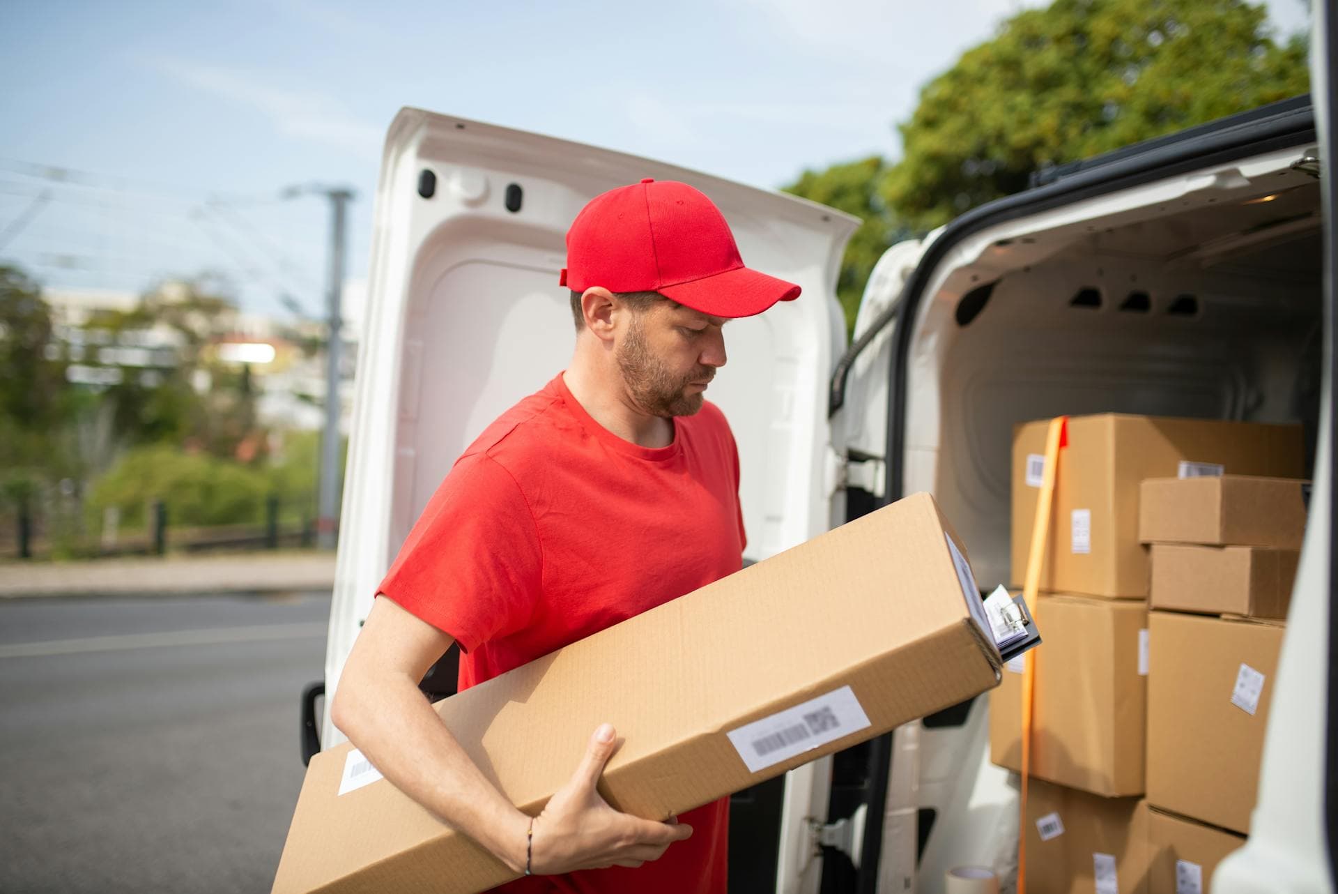 Courier in red uniform unloading packages from delivery van on a bright day — Infinity Logistics parcel delivery